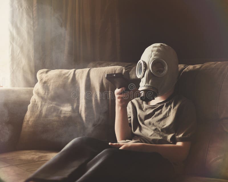 A young child is wearing a gas mask with a remote control watching television on a couch with smoke and pollution for a clean air concept. A young child is wearing a gas mask with a remote control watching television on a couch with smoke and pollution for a clean air concept.