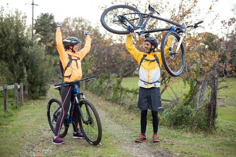 Bärande mountainbike för manlig cyklist medan kvinnlig cyklist som hurrar honom royaltyfri foto Bärande mountainbike för manlig cyklist medan kvinnlig cyklist som hurrar honom royaltyfri foto