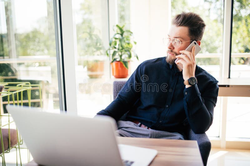Bärtiger Geschäftsmann arbeitet an seinem Laptop in seinem Büro und spricht Telefon und schaut weg stockfoto Bärtiger Geschäftsmann arbeitet an seinem Laptop in seinem Büro und spricht Telefon und schaut weg stockfoto