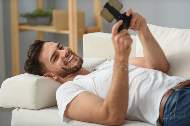 Bärtiger Kerl, der mit Telefon auf einer Couch liegt lizenzfreies stockfoto Bärtiger Kerl, der mit Telefon auf einer Couch liegt lizenzfreies stockfoto