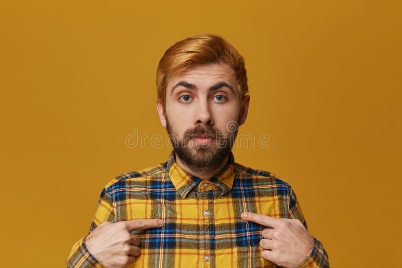 Bärtiger Mann der jungen Rothaarigen trägt karierten gelben verwirrten und überraschten Punkt des Hemdes mit einem Finger auf sei lizenzfreies stockbild Bärtiger Mann der jungen Rothaarigen trägt karierten gelben verwirrten und überraschten Punkt des Hemdes mit einem Finger auf sei lizenzfreies stockbild