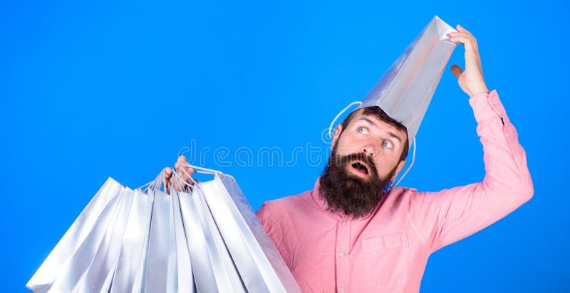 Bärtiger Mann mit tragender Papiertüte des verzögerten Gesichtes und des offenen Munds auf seinem Kopf Shopaholic, das über hohe lizenzfreie stockfotografie Bärtiger Mann mit tragender Papiertüte des verzögerten Gesichtes und des offenen Munds auf seinem Kopf Shopaholic, das über hohe lizenzfreie stockfotografie