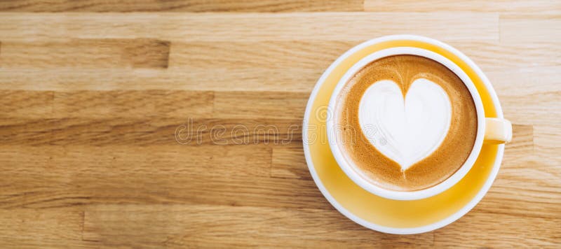 B? sta sikt av den varma cappuccinokaffekoppen p? tr? magasinet med hj? rtalattekonst p? tabellen p? kaf? -, banerformatmat och dr royaltyfria bilder?