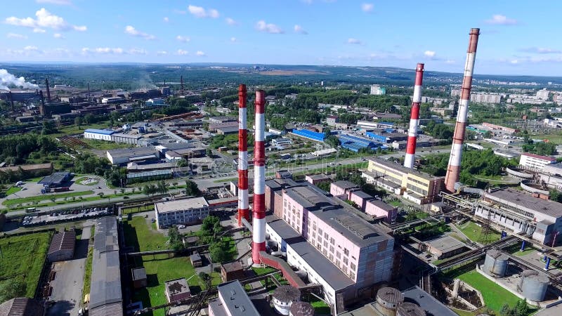 Top view of industrial area of city and plant with red and white pipes. Panorama of city with factories and plants stretching to horizon with blue sky. Concept of industry in urban environment. Top view of industrial area of city and plant with red and white pipes. Panorama of city with factories and plants stretching to horizon with blue sky. Concept of industry in urban environment.