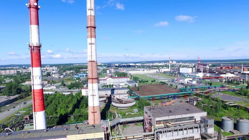 Top view of industrial area of city and plant with red and white pipes. Panorama of city with factories and plants stretching to horizon with blue sky. Concept of industry in urban environment. Top view of industrial area of city and plant with red and white pipes. Panorama of city with factories and plants stretching to horizon with blue sky. Concept of industry in urban environment.