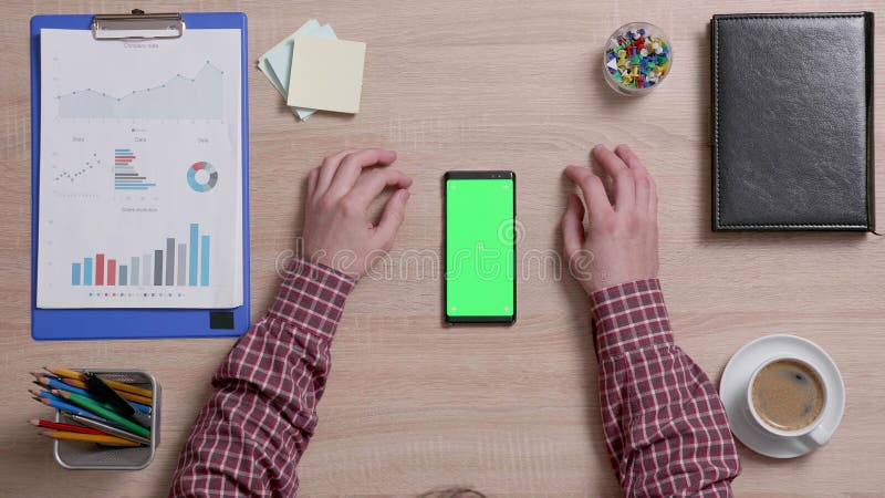 Bästa sikt av manliga händer som bläddrar på den bästa kanten av en smart telefon med den gröna skärmen på