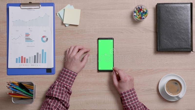 Bästa sikt av manliga händer som bläddrar på den nedersta kanten av en smart telefon med den gröna skärmen på