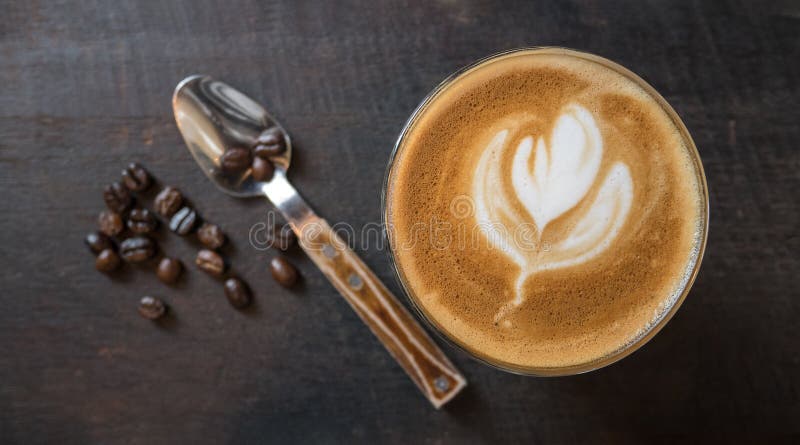 Bästa sikt av varm form för blomma för kaffelattekonst med sked- och kaffebönor på wood tabellbakgrund arkivbild