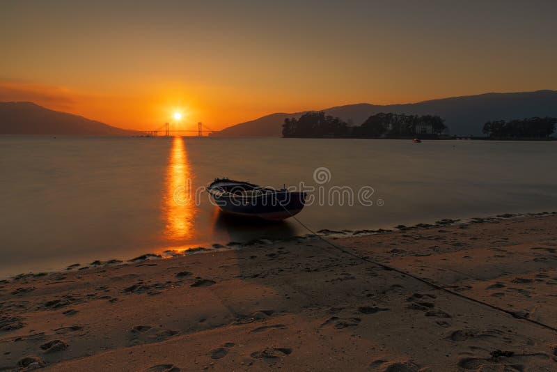 Båt på stranden av cesantes med bron som brinner i bakgrunden vid solnedgången
