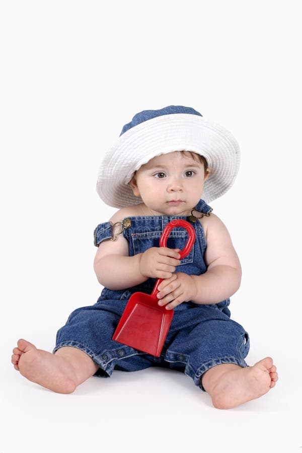 Baby dressed in denim overalls and matching sunhat holding a spade. Baby dressed in denim overalls and matching sunhat holding a spade