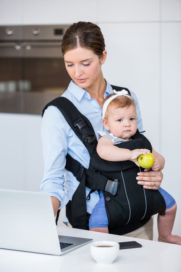 Bébé de transport de femme tout en travaillant dans l'ordinateur portable image libre de droits Bébé de transport de femme tout en travaillant dans l'ordinateur portable image libre de droits