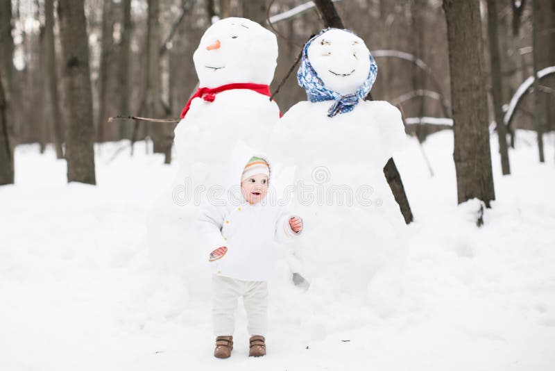 Bébé drôle à côté d'un bonhomme de neige en parc d'hiver images libres de droits Bébé drôle à côté d'un bonhomme de neige en parc d'hiver images libres de droits