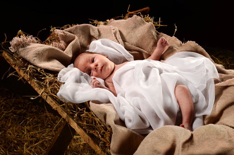 Baby Jesus when born on a manger wrapped in swaddling clothes over dark background. Baby Jesus when born on a manger wrapped in swaddling clothes over dark background