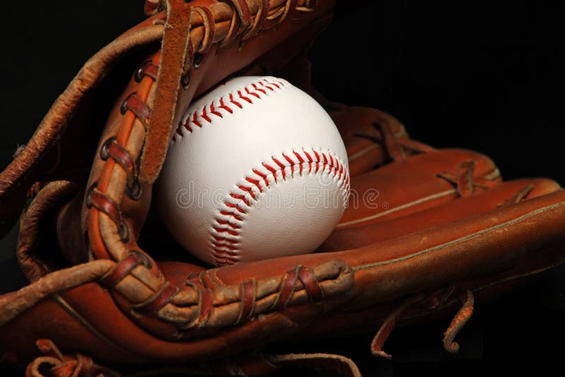 Clean, new baseball inside a leather catcher's glove in black background. Clean, new baseball inside a leather catcher's glove in black background.