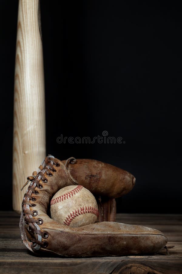 A vintage baseball and old leather mitt on wood surface with wooden bat hanging in background. A vintage baseball and old leather mitt on wood surface with wooden bat hanging in background