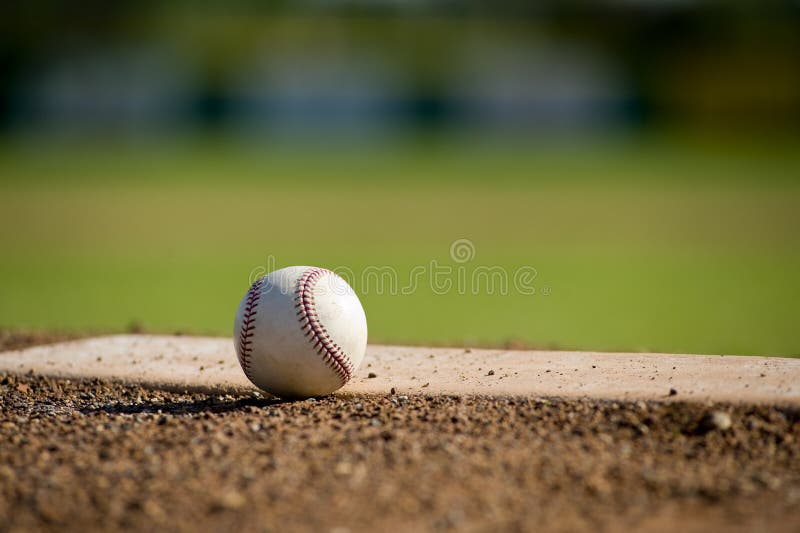 A white leather baseball lying on top of the pitcher's mound at a baseball field with copy space. A white leather baseball lying on top of the pitcher's mound at a baseball field with copy space