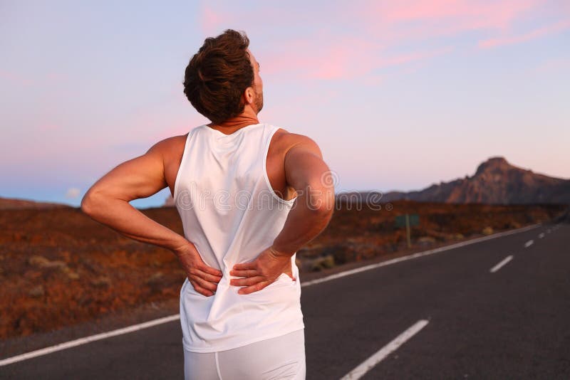 Back pain. Athletic running man with injury in sportswear rubbing touching lower back muscles standing on road outside at night. Back pain. Athletic running man with injury in sportswear rubbing touching lower back muscles standing on road outside at night.