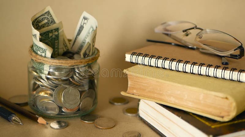 Böcker med den glass encentmyntet skorrar fyllt med mynt och sedlar Skolavgift- eller utbildningsfinansieringbegrepp Stipendiumpe