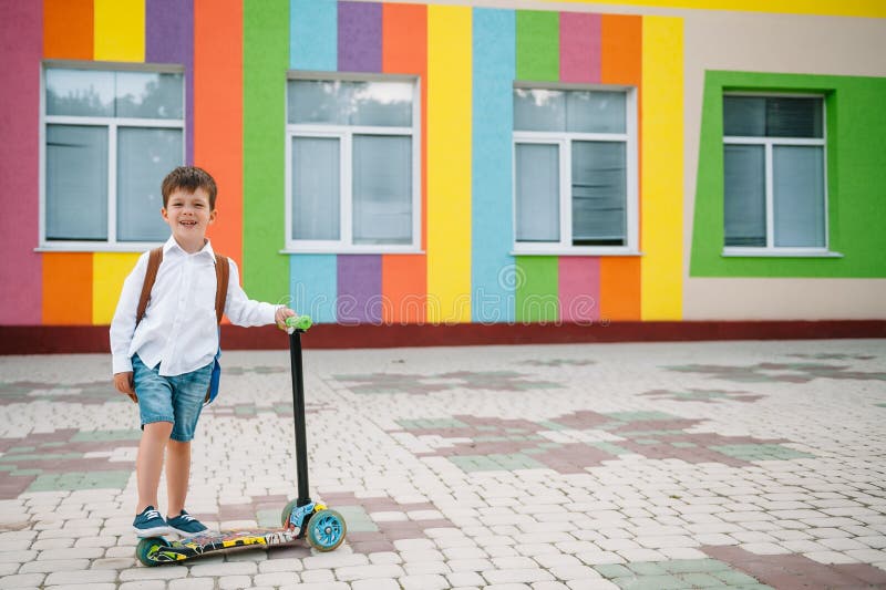 Băiat adolescent cu scuter cu piciorul în apropierea școlii moderne. copil cu rucsac și cărți în aer liber. începutul lecțiilor. p royalty free stock photography