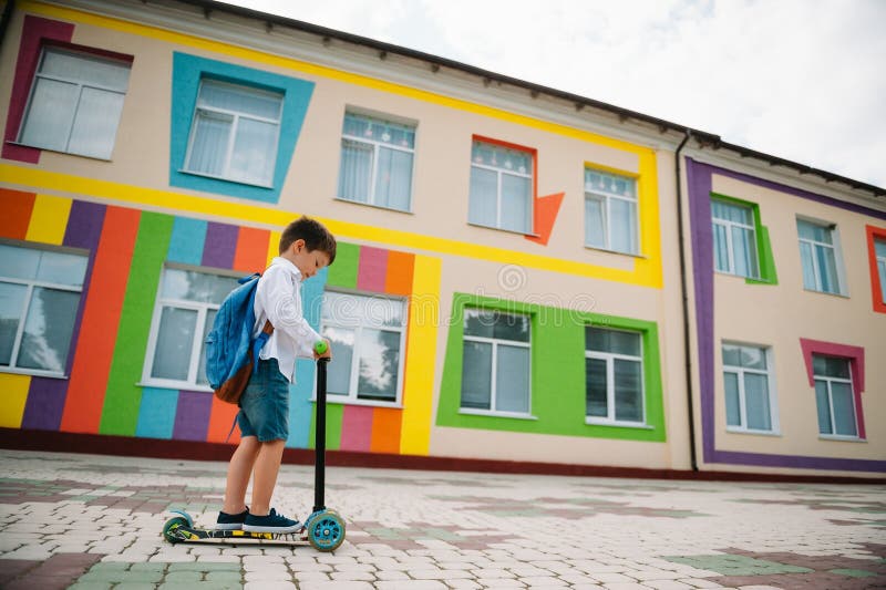Băiat adolescent cu scuter cu piciorul în apropierea școlii moderne. copil cu rucsac și cărți în aer liber. începutul lecțiilor. p royalty free stock photography