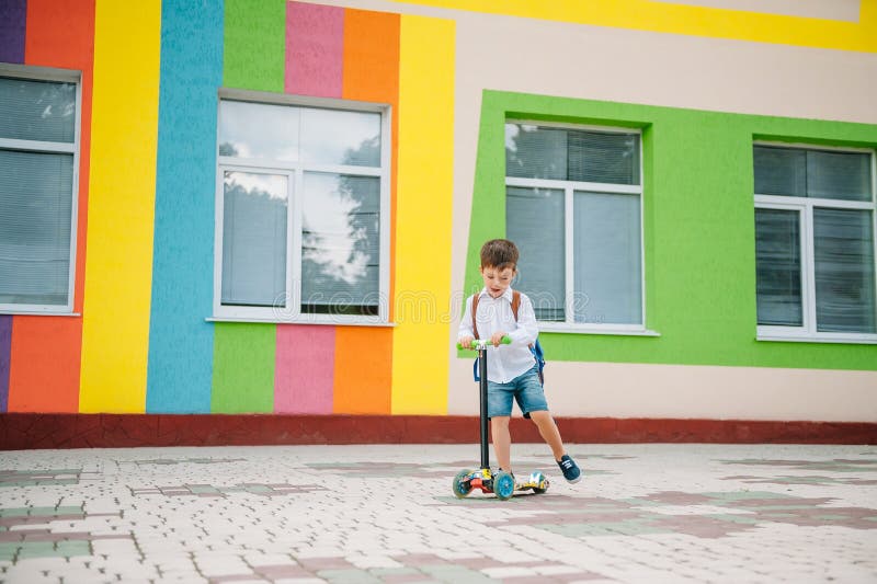 Băiat adolescent cu scuter cu piciorul în apropierea școlii moderne. copil cu rucsac și cărți în aer liber. începutul lecțiilor. p stock photo