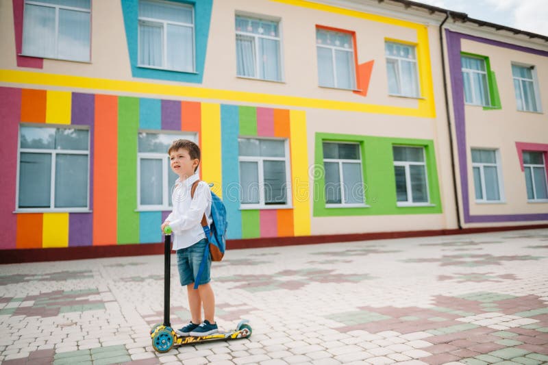 Băiat adolescent cu scuter cu piciorul în apropierea școlii moderne. copil cu rucsac și cărți în aer liber. începutul lecțiilor. p stock photo