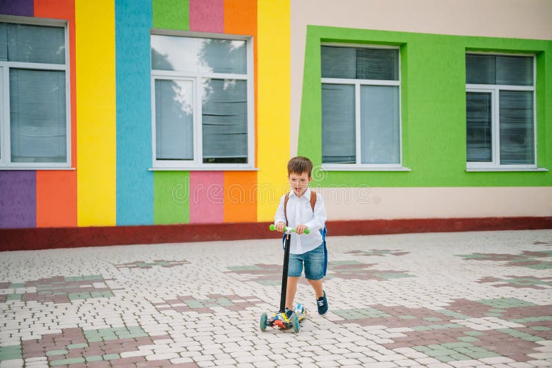 Băiat adolescent cu scuter cu piciorul în apropierea școlii moderne. copil cu rucsac și cărți în aer liber. începutul lecțiilor. p stock photography