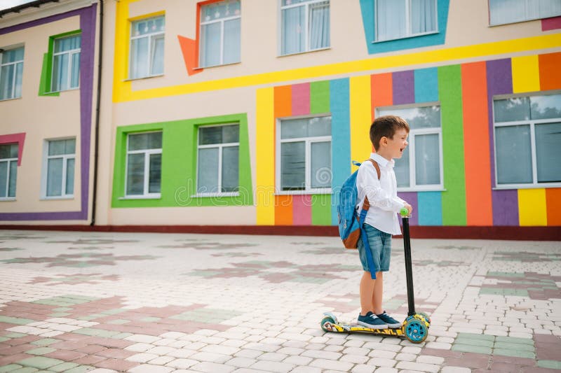 Băiat adolescent cu scuter cu piciorul în apropierea școlii moderne. copil cu rucsac și cărți în aer liber. începutul lecțiilor. p royalty free stock photos