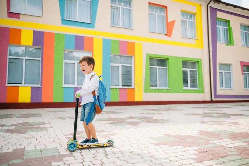 Băiat adolescent cu scuter cu piciorul în apropierea școlii moderne. copil cu rucsac și cărți în aer liber. începutul lecțiilor. p royalty free stock photo