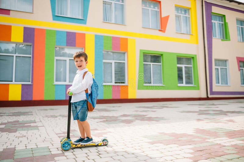 Băiat adolescent cu scuter cu piciorul în apropierea școlii moderne. copil cu rucsac și cărți în aer liber. începutul lecțiilor. p royalty free stock image