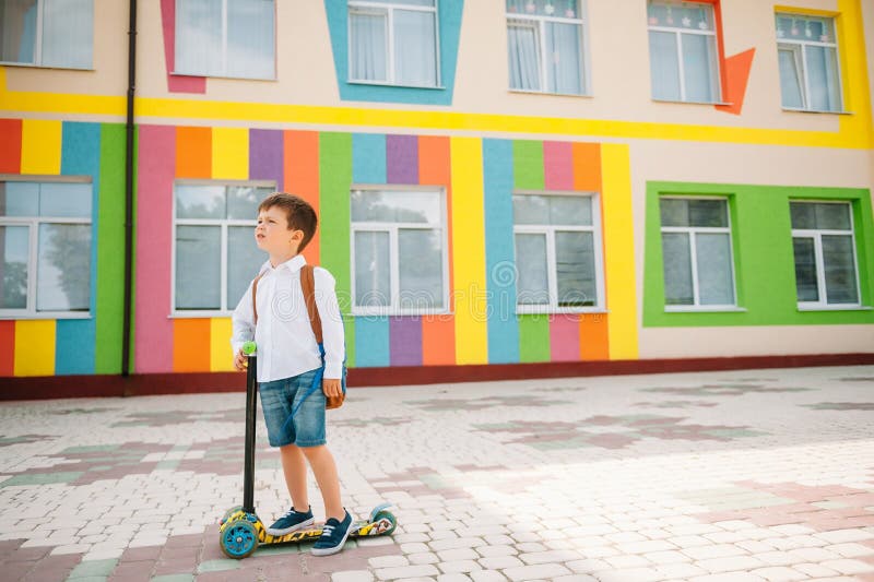 Băiat adolescent cu scuter cu piciorul în apropierea școlii moderne. copil cu rucsac și cărți în aer liber. începutul lecțiilor. p stock photos