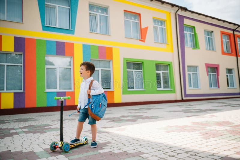 Băiat adolescent cu scuter cu piciorul în apropierea școlii moderne. copil cu rucsac și cărți în aer liber. începutul lecțiilor. p stock photo