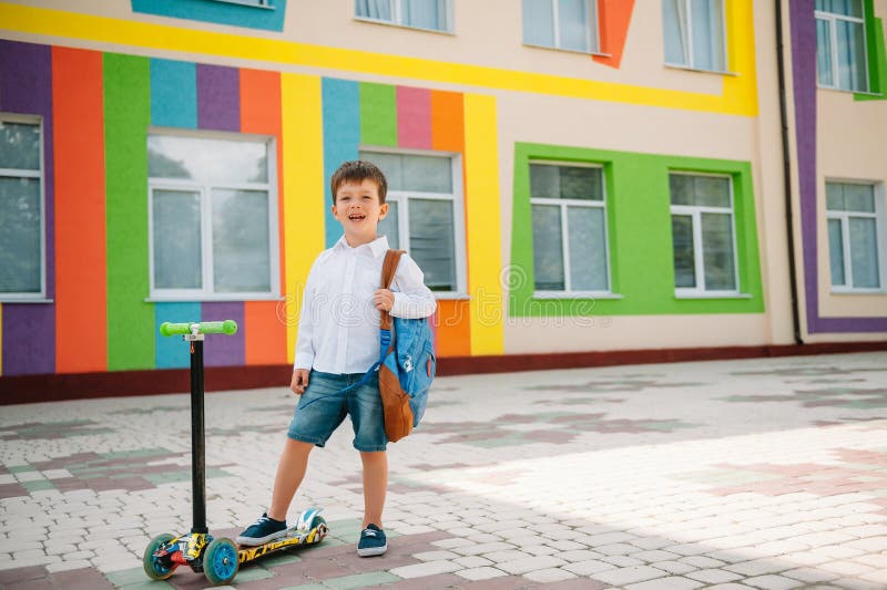 Băiat adolescent cu scuter cu piciorul în apropierea școlii moderne. copil cu rucsac și cărți în aer liber. începutul lecțiilor. p stock images