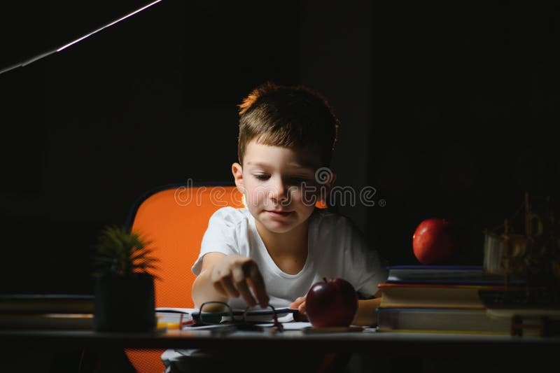 Băiatul învață lecții de acasă la masă în lumina unei lămpi de masă stock photography