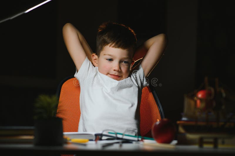 Băiatul învață lecții de acasă la masă în lumina unei lămpi de masă stock photos