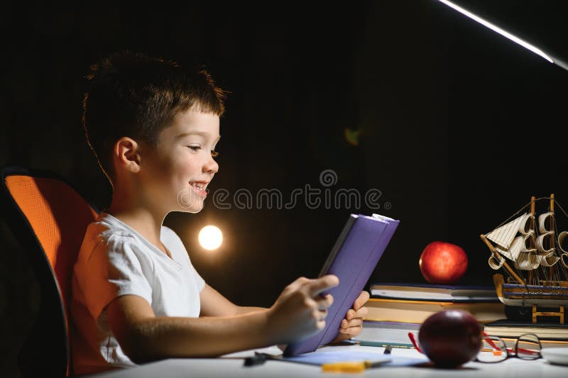Băiatul învață lecții de acasă la masă în lumina unei lămpi de masă stock images