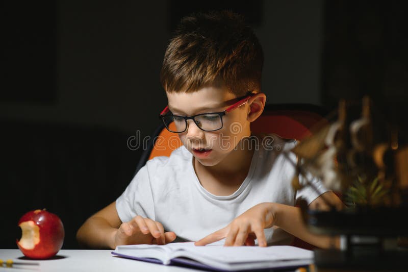Băiatul învață lecții de acasă la masă în lumina unei lămpi de masă royalty free stock photography