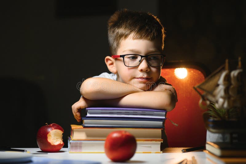 Băiatul învață lecții de acasă la masă în lumina unei lămpi de masă stock photos