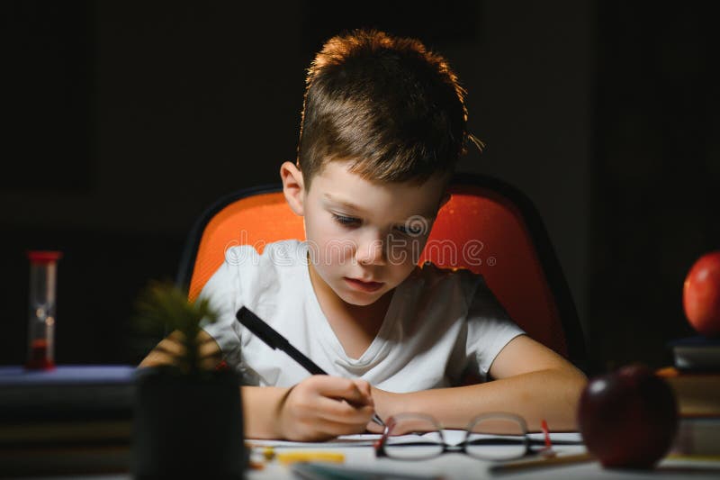 Băiatul învață lecții de acasă la masă în lumina unei lămpi de masă royalty free stock image