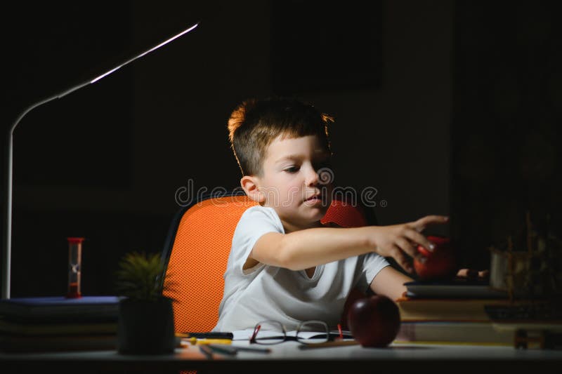 Băiatul învață lecții de acasă la masă în lumina unei lămpi de masă royalty free stock images