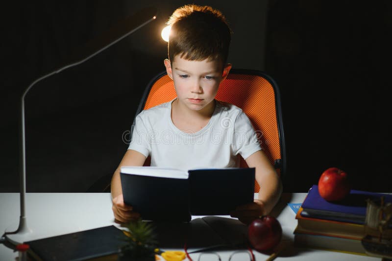 Băiatul învață lecții de acasă la masă în lumina unei lămpi de masă royalty free stock photo