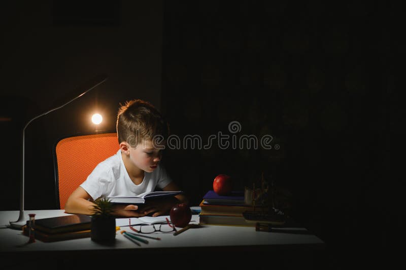 Băiatul învață lecții de acasă la masă în lumina unei lămpi de masă stock photography