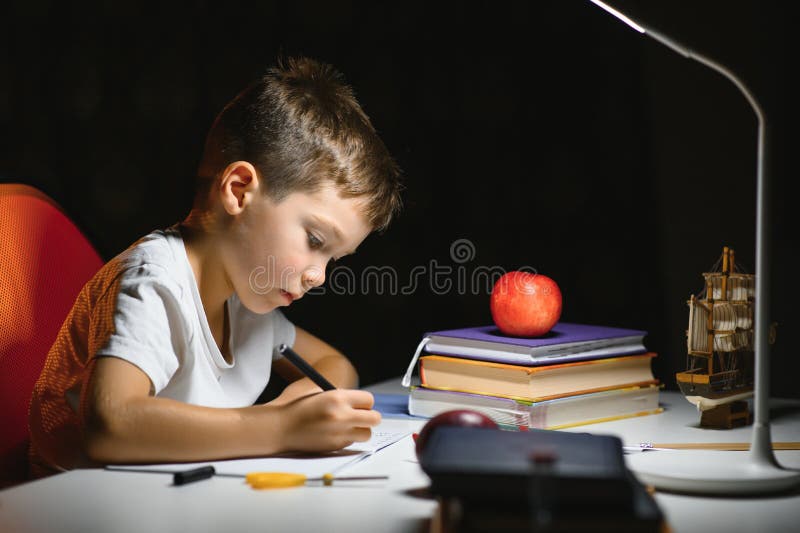 Băiatul învață lecții de acasă la masă în lumina unei lămpi de masă royalty free stock photos