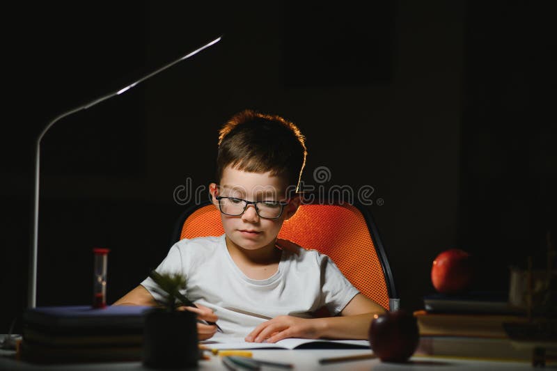Băiatul învață lecții de acasă la masă în lumina unei lămpi de masă royalty free stock photo