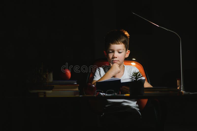 Băiatul învață lecții de acasă la masă în lumina unei lămpi de masă royalty free stock images