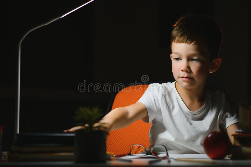 Băiatul învață lecții de acasă la masă în lumina unei lămpi de masă royalty free stock photos