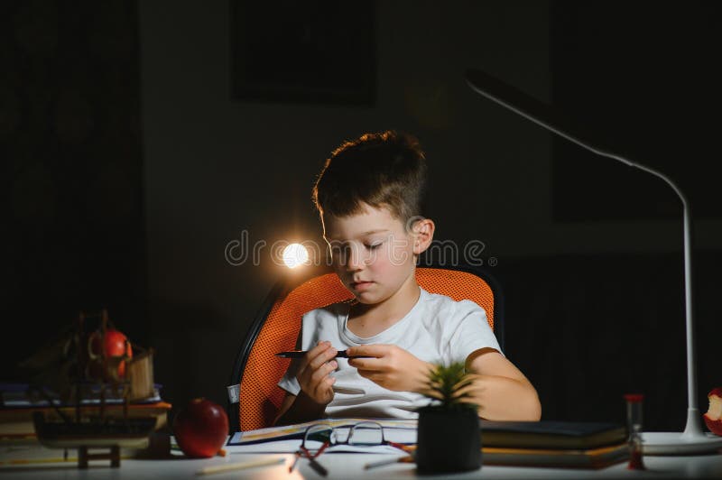 Băiatul învață lecții de acasă la masă în lumina unei lămpi de masă royalty free stock images