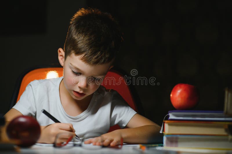 Băiatul învață lecții de acasă la masă în lumina unei lămpi de masă royalty free stock photography