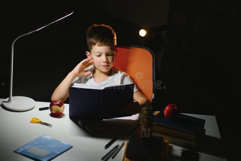 Băiatul învață lecții de acasă la masă în lumina unei lămpi de masă stock image