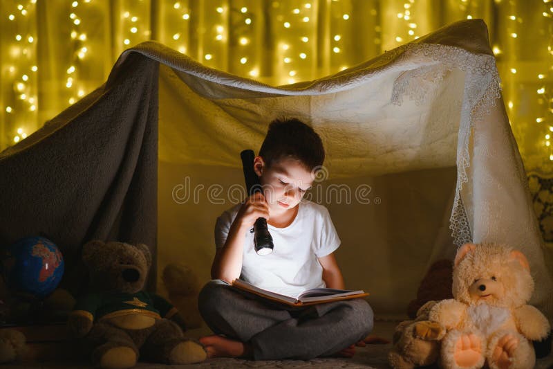 Băiețaș citind cărți în cortul de joacă noaptea stock photo